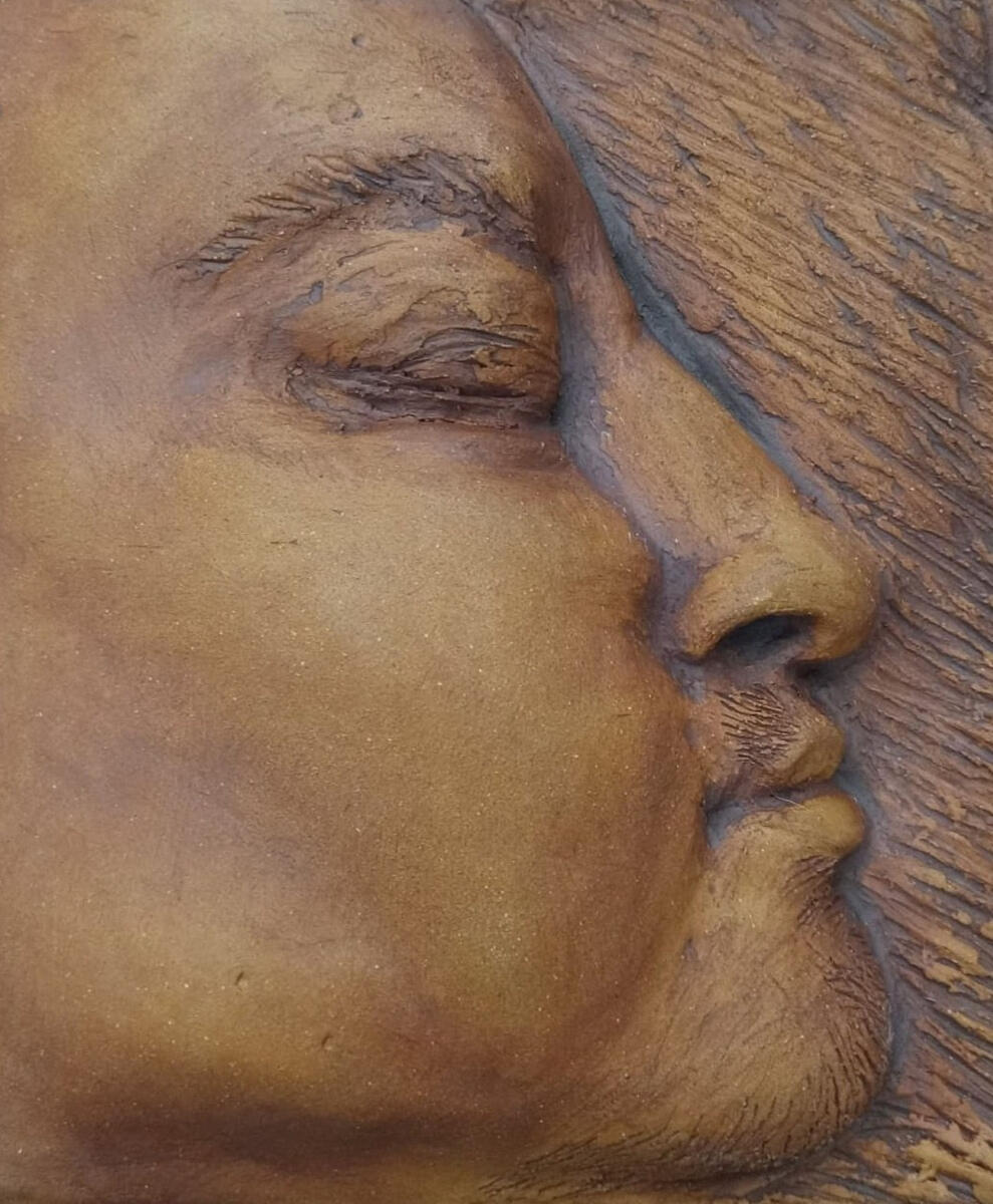 Small bas relief (ceramic tile) of a nonbinary person's facial profile by Shane Brodie. Eyes are closed. Surface texture such hair and wrinkles are emphasized by dark reddish brown iron oxide.
