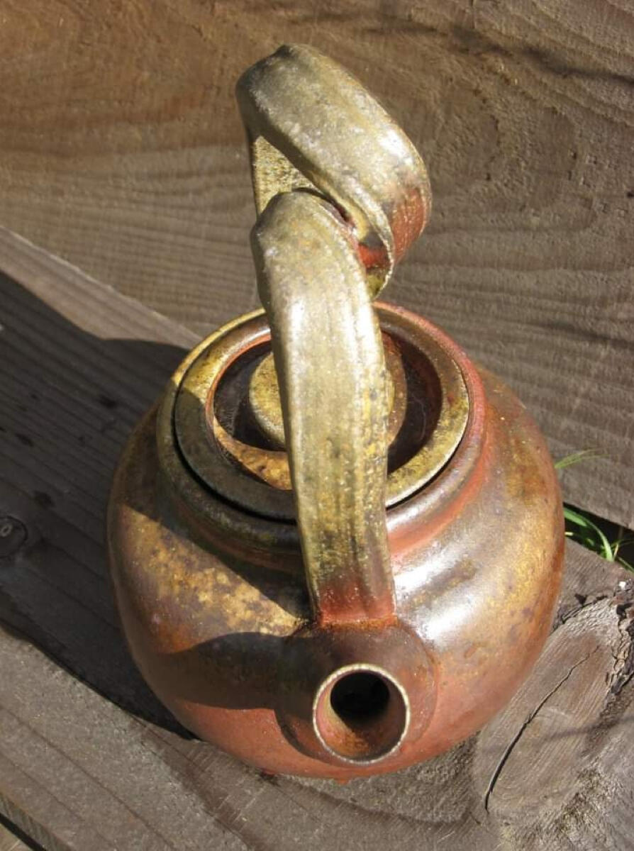 Woodfired stoneware teapot made by Shane Brodie with a mottled red and tan surface created from the wood ash. The oversized handle has a large looping twist in it.