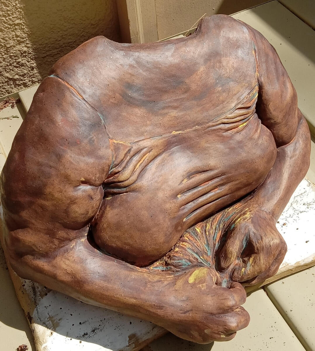 Ceramic sculpture of the torso and arms of a queer woman by Shane Brodie. Her hands are in front and pulling something coming from her torso. Wrinkles and folds are emphasized by the application of multiple stains.