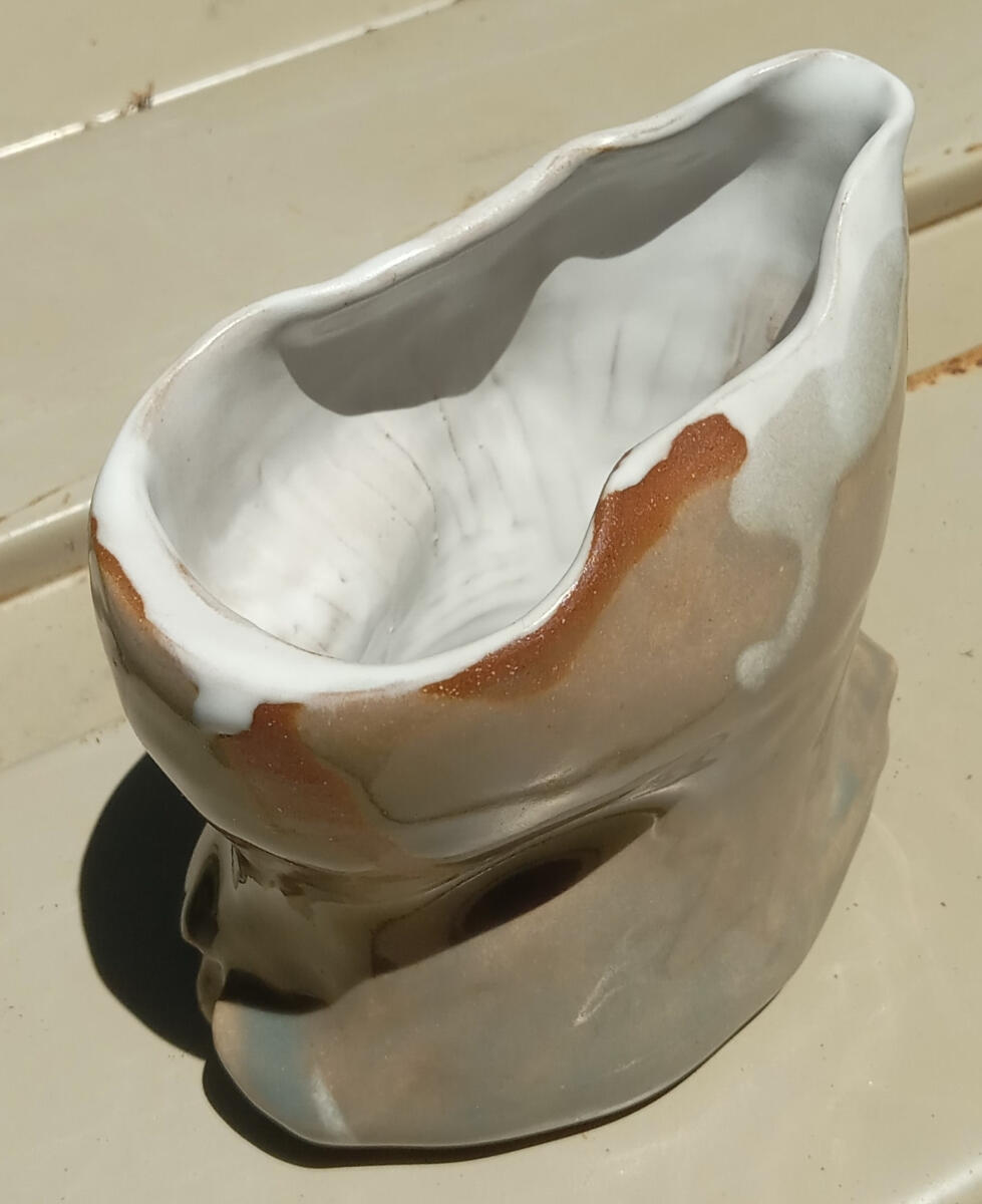 Handle-less, dimpled stoneware creamer by Shane Brodie. There is a depression running around the outside of the piece for holding and pouring. Glazed light green with a white liner.