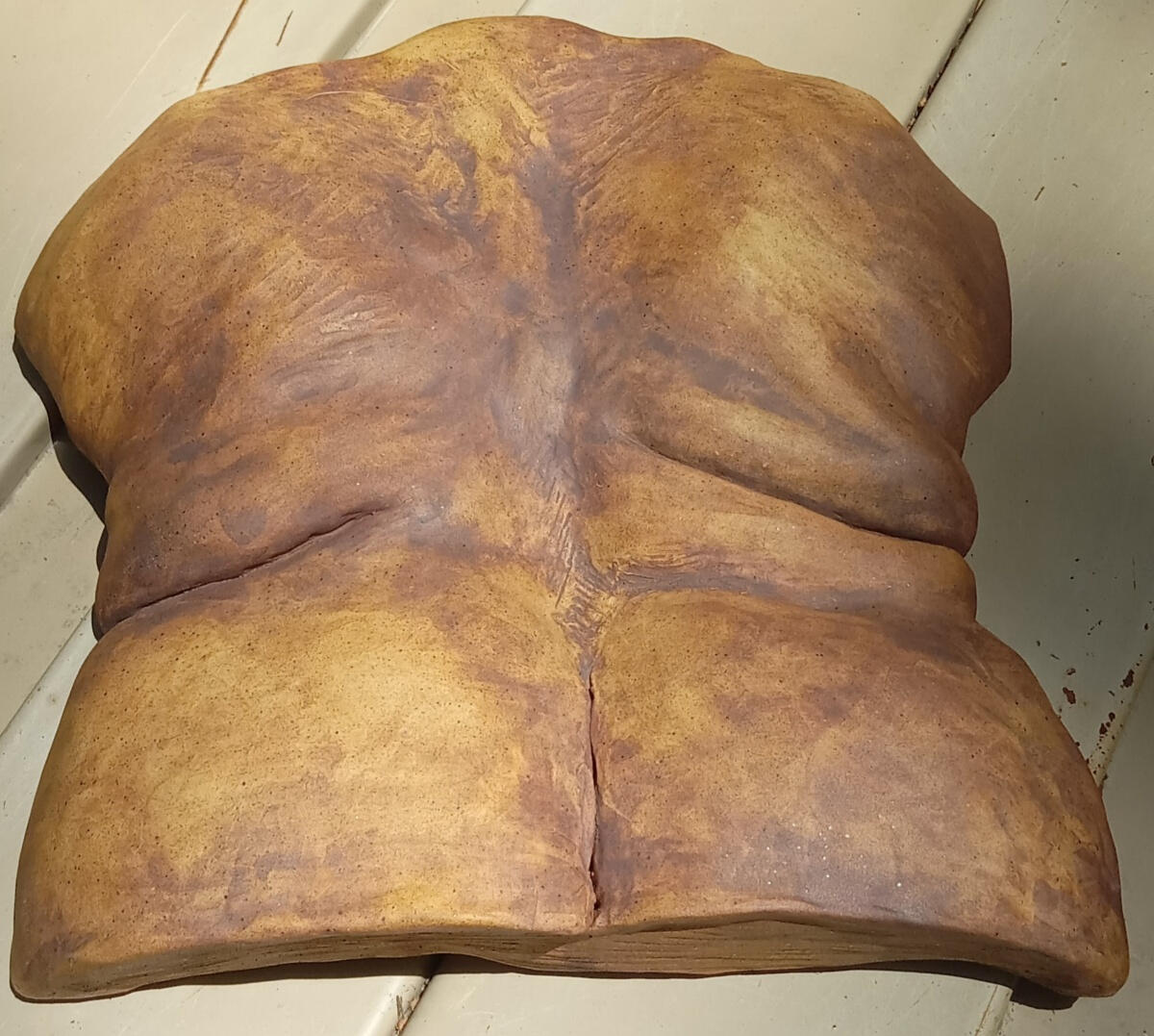 Ceramic bas relief sculpture of a queer woman's shoulders, back and hips with ample skin folds by Shane Brodie. Surface has a subtle texture emphasized by application of reddish-brown iron oxide and yellow rutile.