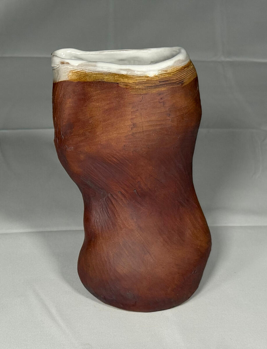 Tall, handle-less, stoneware pitcher with a defined spout throat by Shane Brodie. The heavily striated surface is unglazed, but is a rusty red from iron oxide staining. The inside and rim are covered with a white glaze.