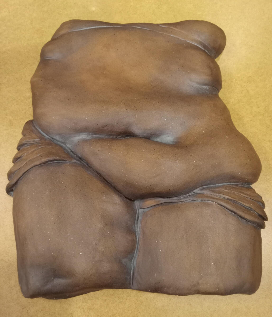 Ceramic bas relief sculpture of a nonbinary person's torso and thighs by Shane Brodie. Surface is very smooth and burnished. Wrinkles and folds in fabric or skin are emphasized by the application of iron oxide to the piece.